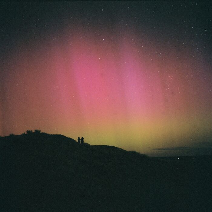 Rare aurora borealis lighting the night sky over a hill with silhouetted people watching