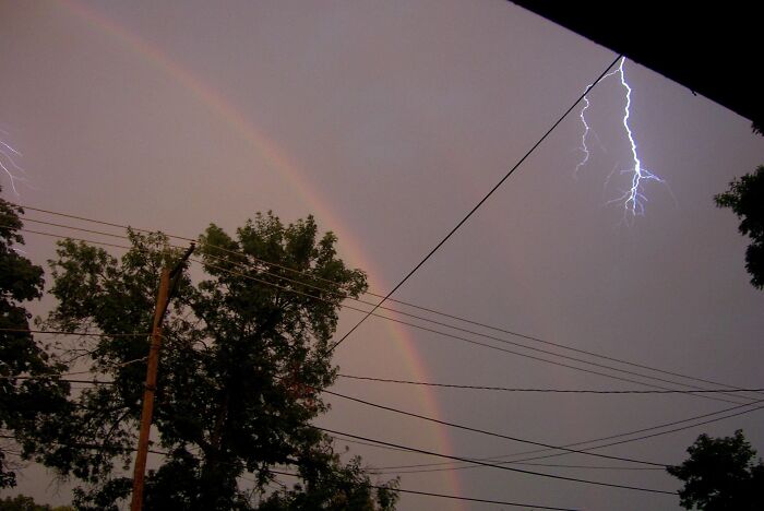Rare moment capturing lightning strikes alongside a faint double rainbow at dusk