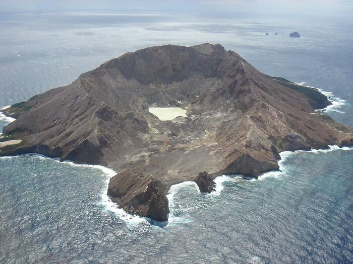 Aerial view of a volcanic island surrounded by ocean with rugged rocky terrain