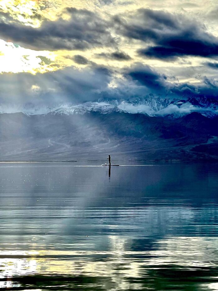 Person paddleboarding on calm lake with mountains and clouds at rare sunrise