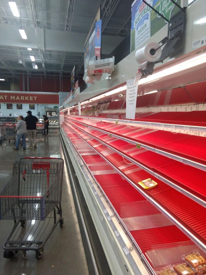 Nearly empty supermarket meat aisle with one tray remaining on red shelves