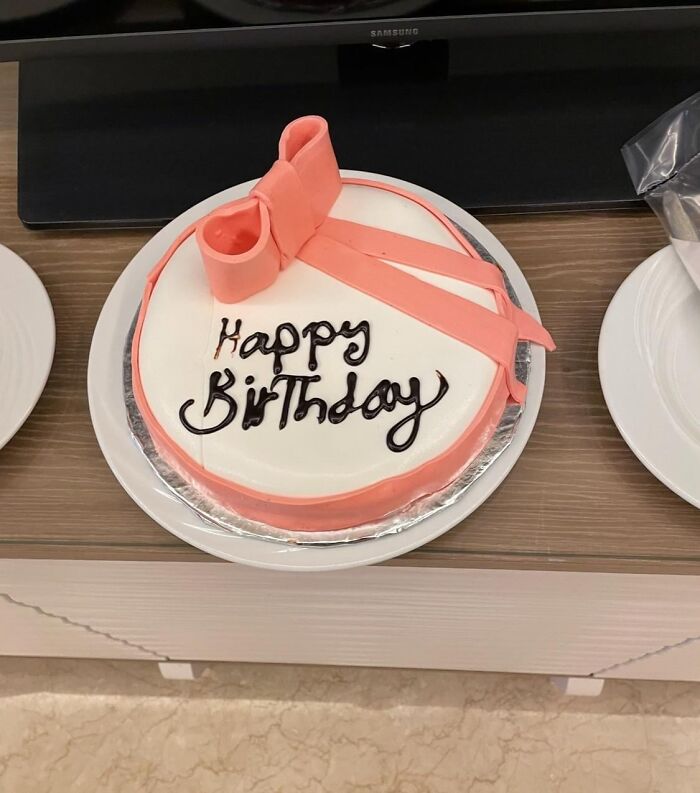 Round birthday cake with pink bow decoration and happy birthday icing