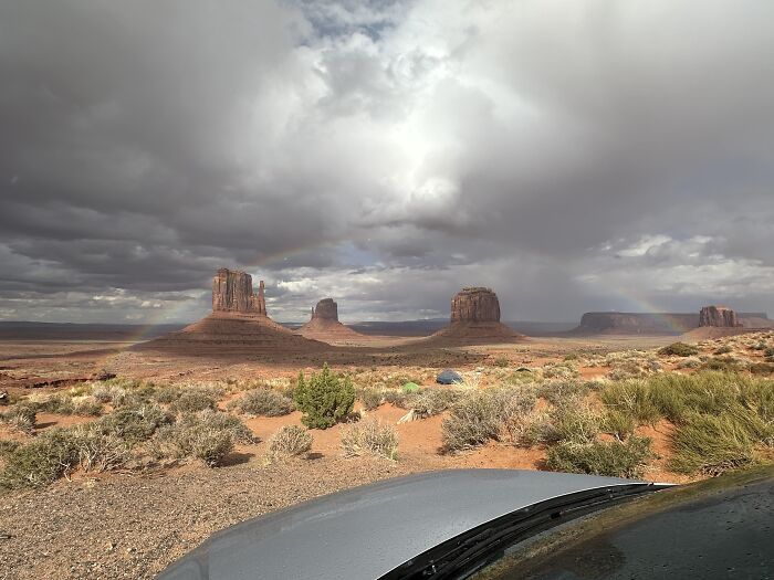 Rainbow appearing over Monument Valley desert landscape with car roof visible