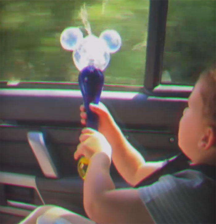 A child in a car holding a Mickey Mouse bubble wand, blowing bubbles outside the window. People find odd details.