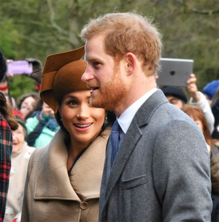 Meghan Markle smiling next to Prince Harry. They are surrounded by people. People pick out odd details.
