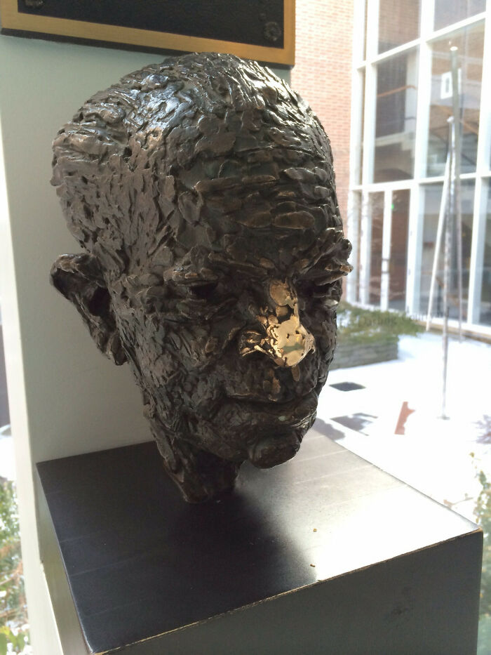 Bronze sculpted bust inside university building with window reflections