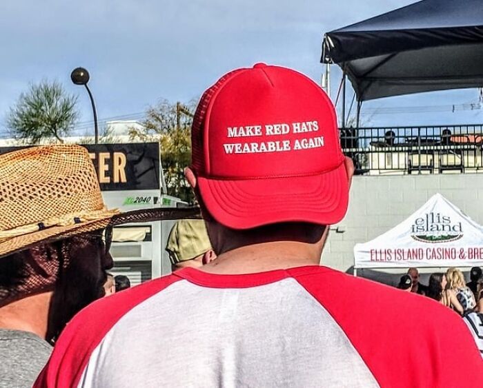 A person wearing a red hat that says MAKE RED HATS WEARABLE AGAIN, revealing a tiny red flag.