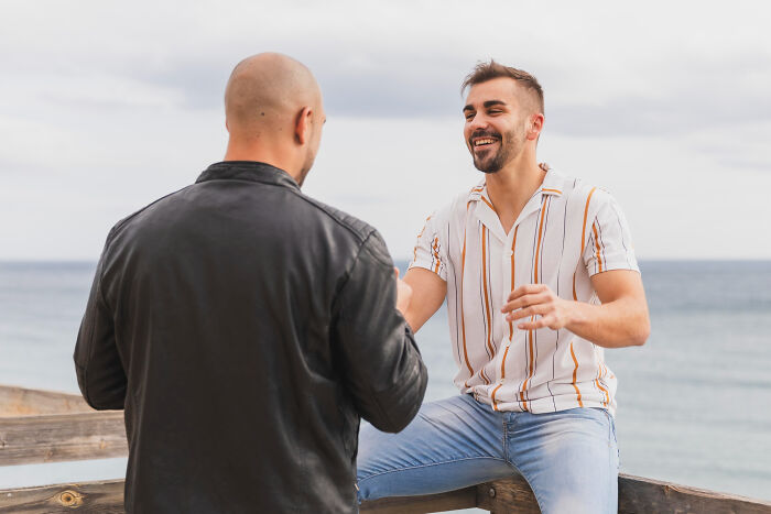 Two men chatting by the sea, one laughing. Reveals more about someone and tiny red flags in conversation.