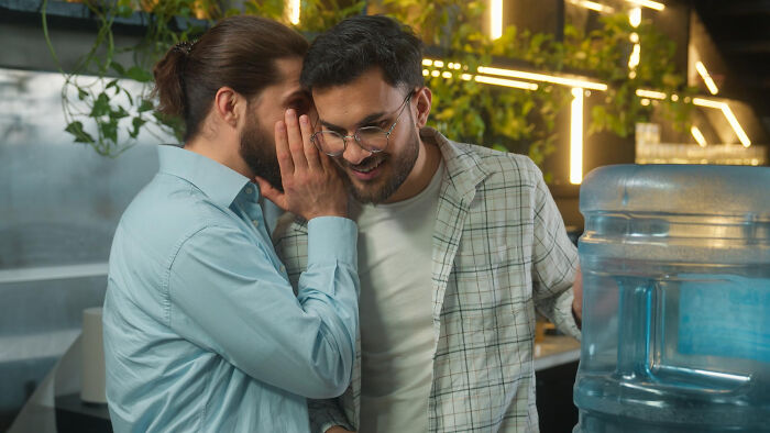 Two men, one whispering a secret to the other, who is smiling. Represents subtle red flags revealing personality.
