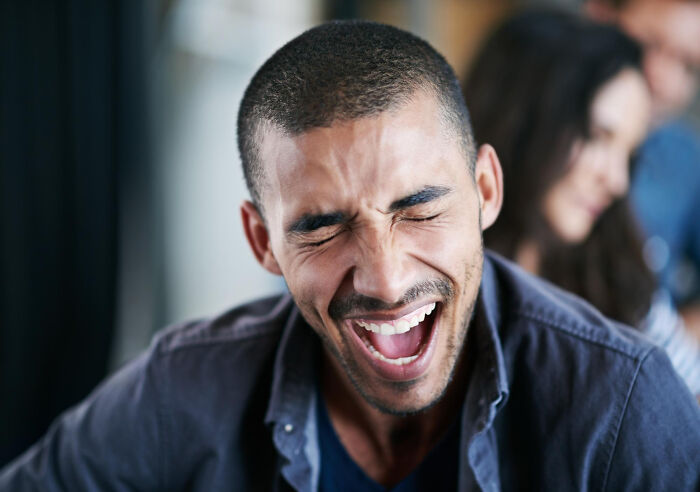 A man with closed eyes and an open mouth, laughing heartily. He reveals more about someone.