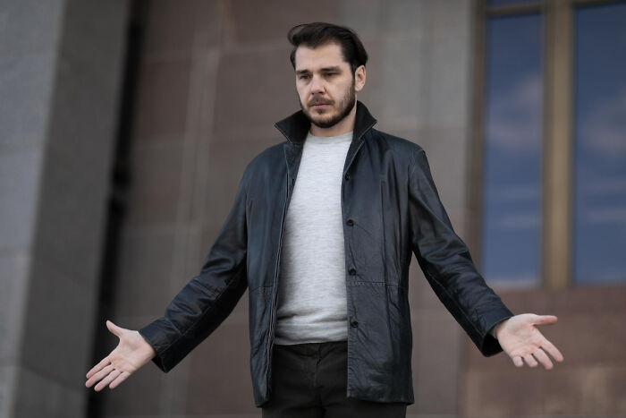 A man with a beard and dark hair wearing a leather jacket and grey shirt, shrugging with open palms, illustrating tiny red flags.