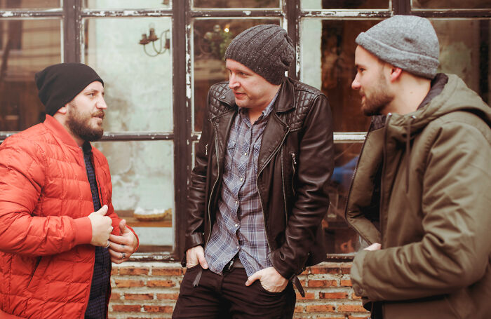 Three men in winter hats and jackets chatting near a window. Their body language might reveal more about someone.