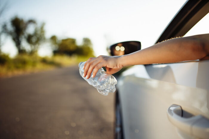 Hand dropping a plastic bottle from a car window onto a road, an example of a tiny red flag behavior revealing more about someone.