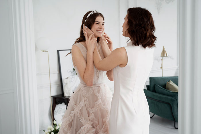 Woman wearing dream wedding dress smiling as another woman adjusts her tiara Woman wearing dream wedding dress smiling as another woman adjusts her tiara