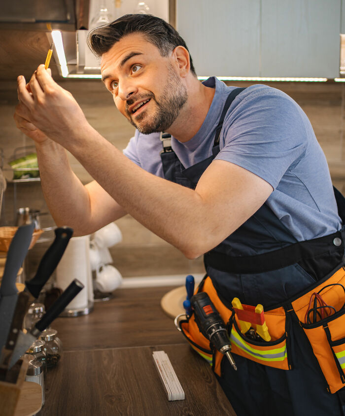 Man installing lights, wearing a tool belt, looking up and smiling. Habits that save you money by DIY.