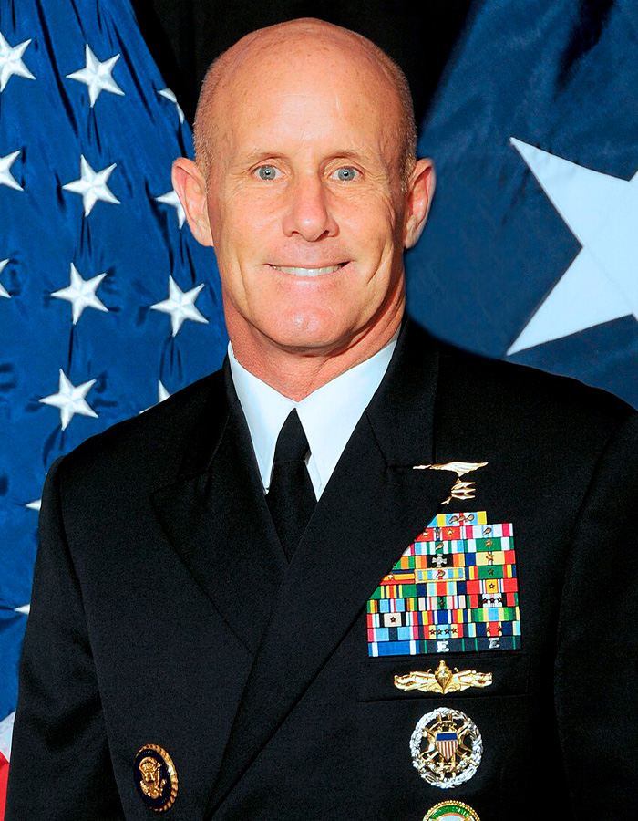 Retired U.S. Navy Vice Admiral in uniform with medals against American flag background Retired U.S. Navy Vice Admiral in uniform with medals against American flag background