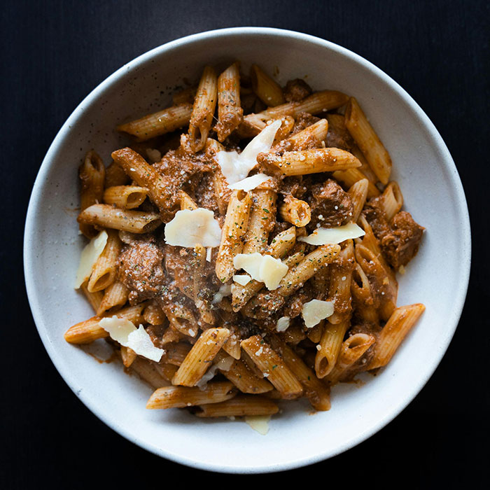 A bowl of penne pasta with meat sauce and shaved parmesan cheese, representing dishes the ultra-rich enjoy.