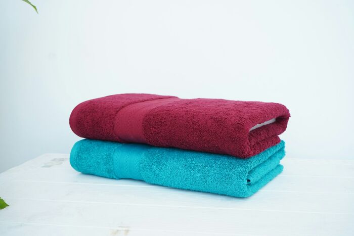 A stack of two plush, folded towels, one maroon and one teal, on a white surface, representing silent luxuries.