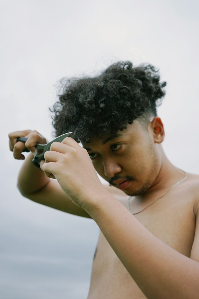 A man with curly hair cutting his own hair, reflecting unexpected wedding drama.