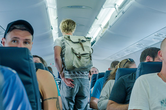 Crowded plane aisle with passengers seated and a person walking down the center