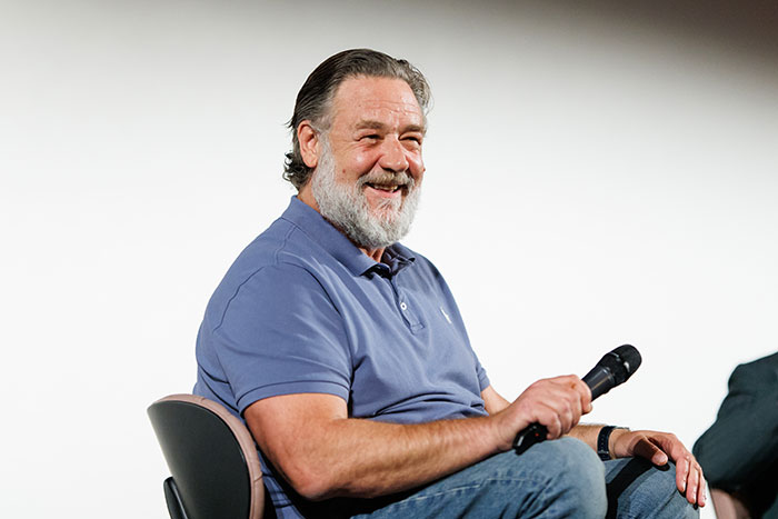 Russell Crowe smiling and holding microphone during talk event Russell Crowe smiling and holding microphone during talk event
