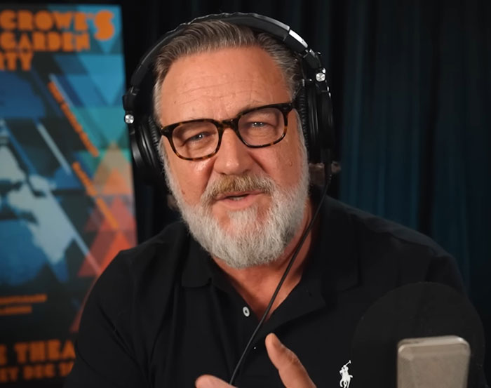Russell Crowe wearing headphones speaking in podcast or radio setup