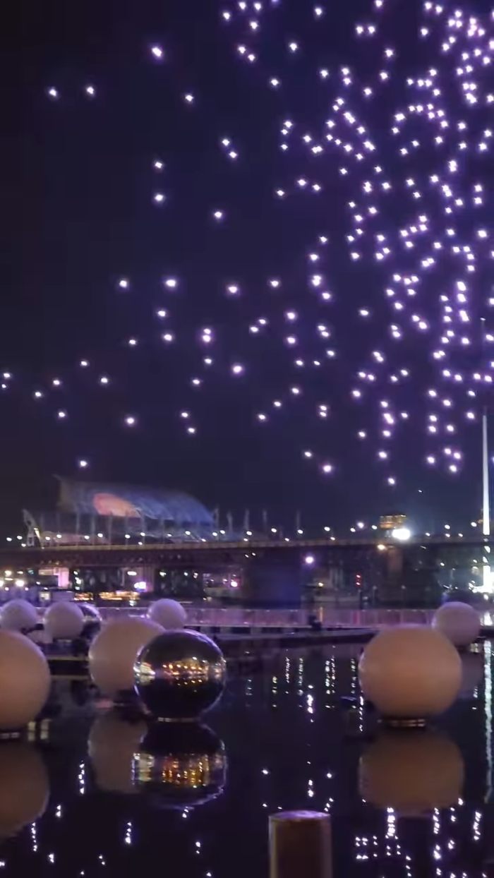 Sydney drone show at night with drones illuminated over harbor near bridge Sydney drone show at night with drones illuminated over harbor near bridge