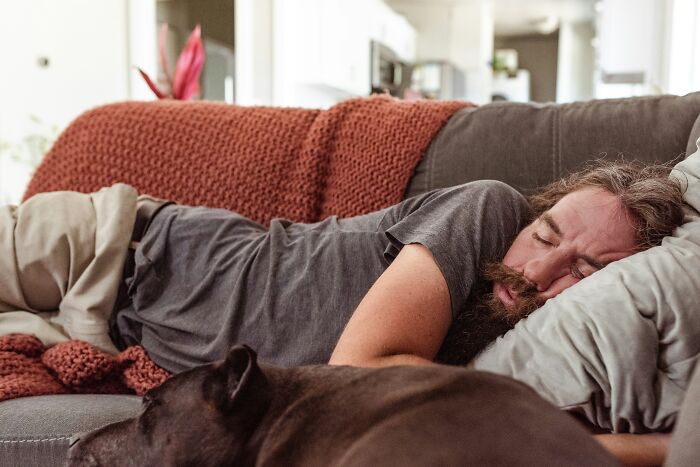 Man with a beard and a dog napping on a couch. Don't overlook health warning signs; consider routine cancer screening.