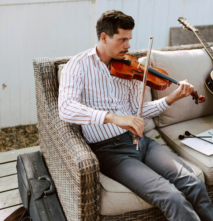 Man playing violin sitting on wicker sofa playing violin music
