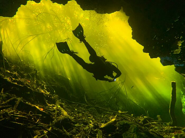 Scuba diver exploring sunlit underwater cave environment