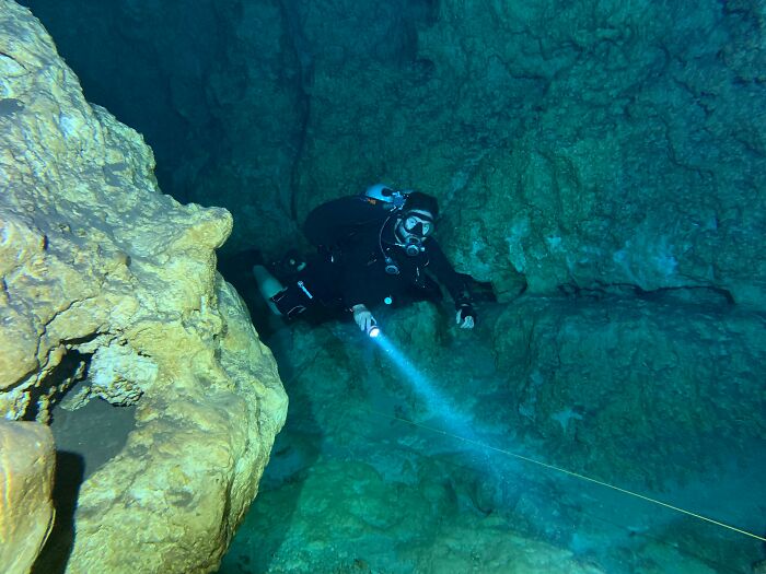 Cave diver navigating rocky passage with flashlight and guide line