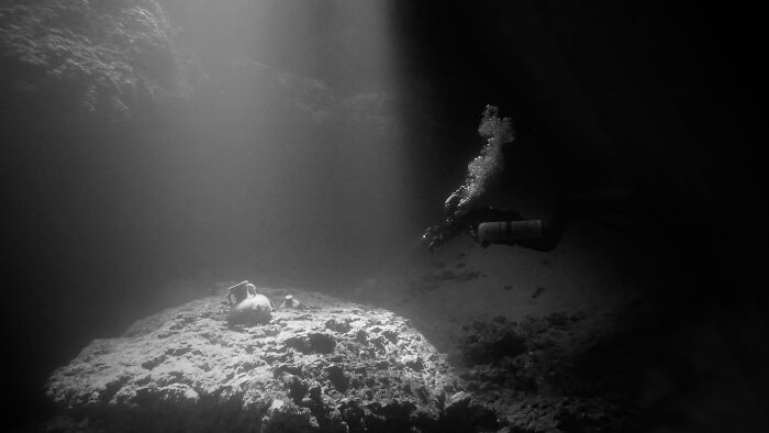 Scuba diver exploring underwater cave illuminated by light beams