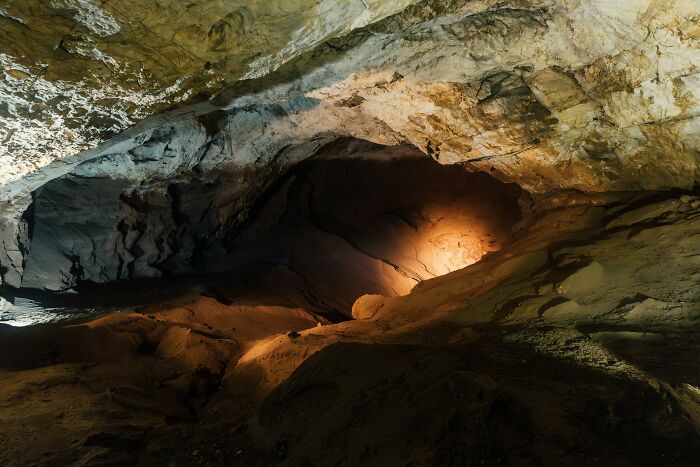 Dimly lit narrow cave interior with rocky walls and uneven floor