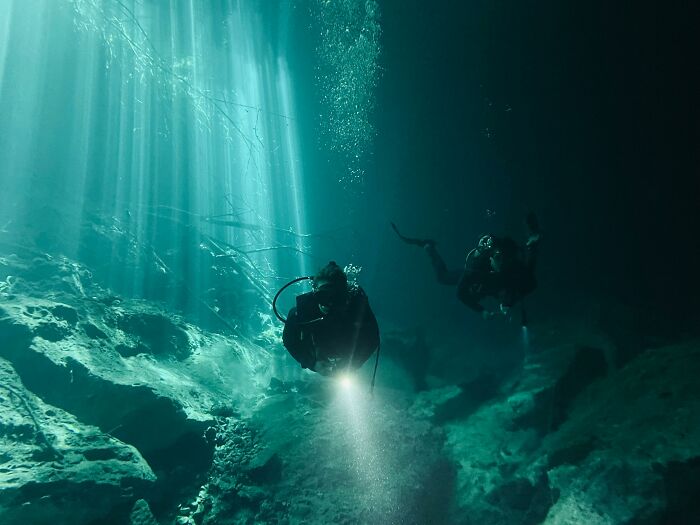 Scuba divers navigating a dark underwater cave illuminated by beams of light