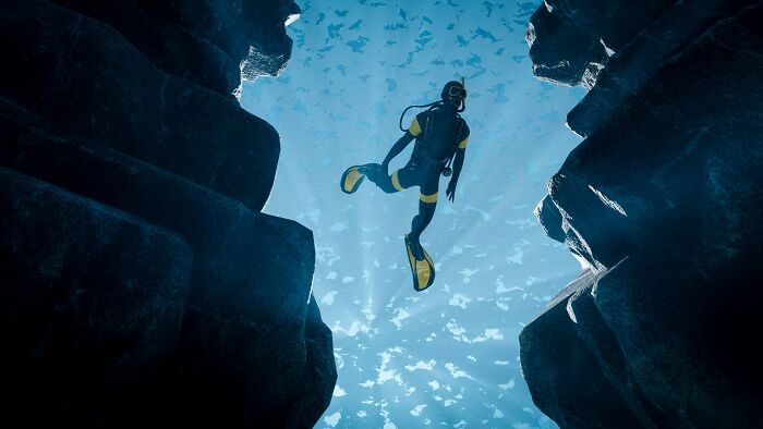 Diver swimming between rock formations in a deep underwater cave