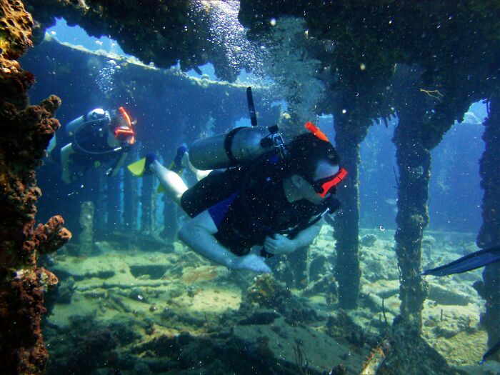 Scuba divers examining an underwater cave with corroded pillars