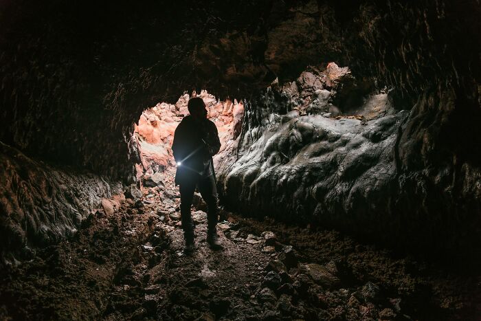Person with flashlight exploring a dark cave corridor with rocky walls