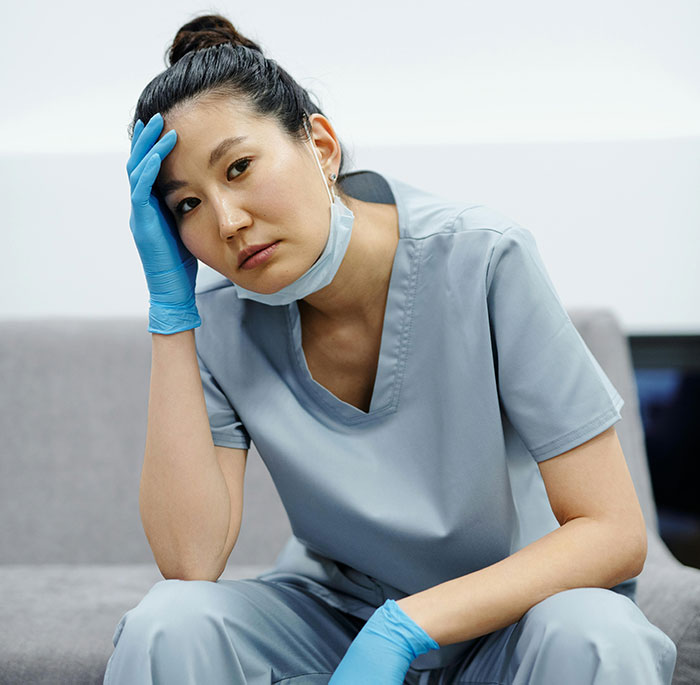 Tired nurse with face mask resting head on hand