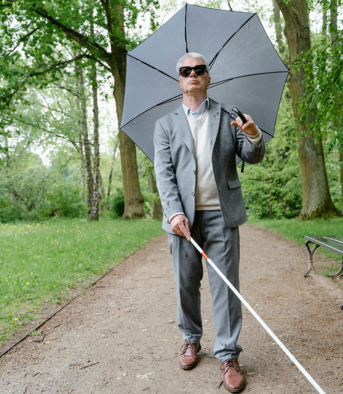 Blind man using white cane walking with umbrella