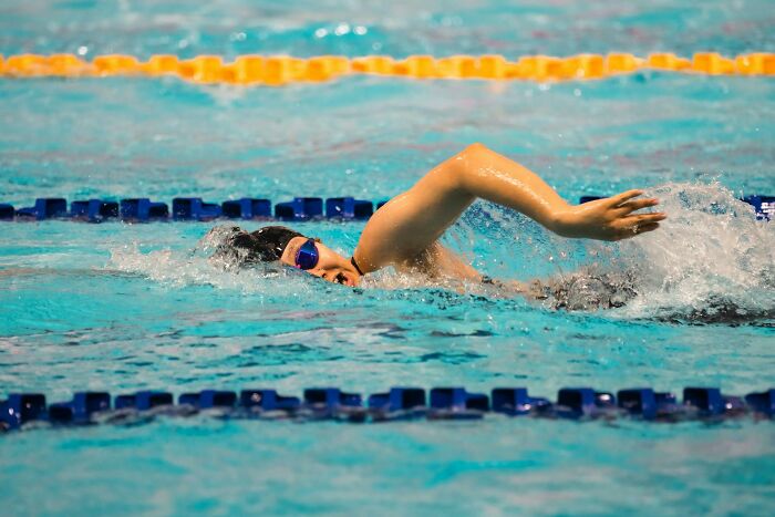 A swimmer in blue goggles and black cap, creating splashes in a pool. Outdated facts can often be debunked like old swimming techniques.