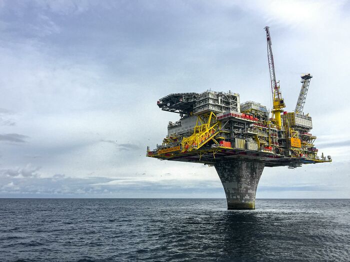 An oil rig against a vast cloudy sky and ocean, a structure that represents outdated facts in an evolving world.