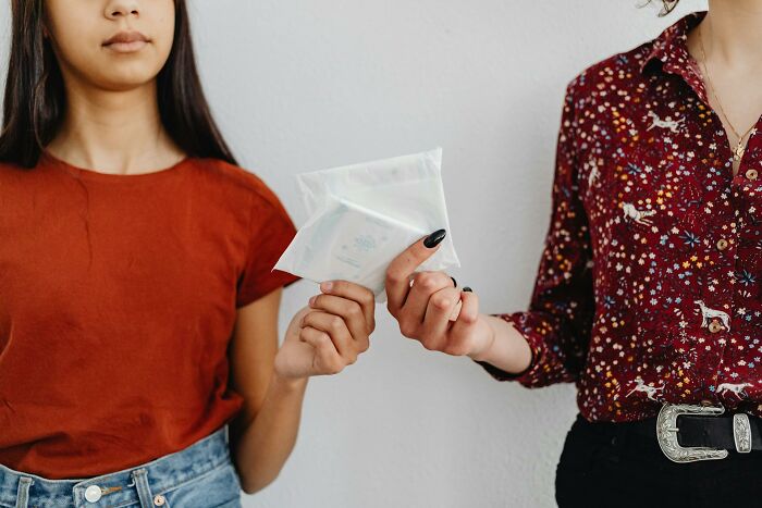 Two women exchanging menstrual pads, dispelling outdated facts about feminine hygiene.