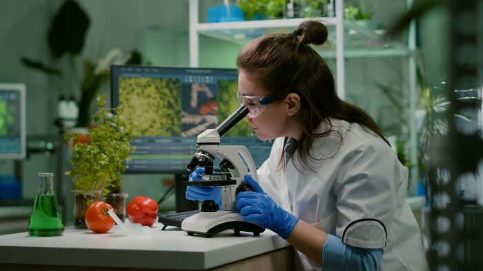 A scientist in a lab coat and safety goggles examining a sample under a microscope to disprove outdated facts.