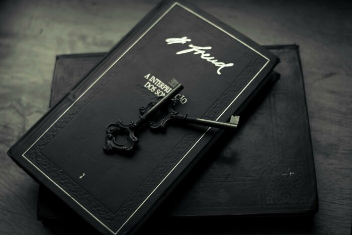 Two dark, antique keys lie atop a closed black book titled Freud, symbolizing unlocking outdated facts and hidden truths.