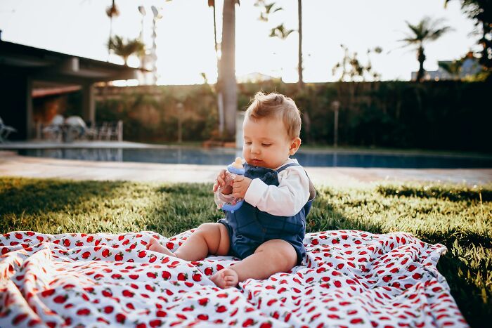 A baby sits on a strawberry blanket outdoors, holding a teething toy. Outdated facts can be misleading.