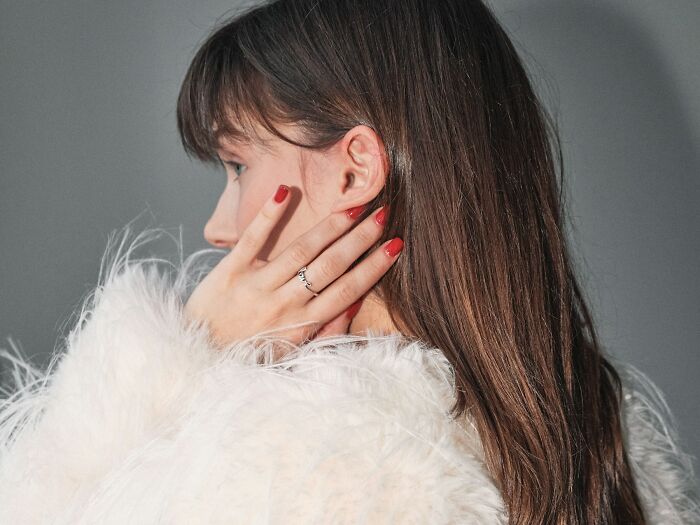 A woman in a white feathery top, with red nails and a ring, poses against a gray background, illustrating outdated facts.