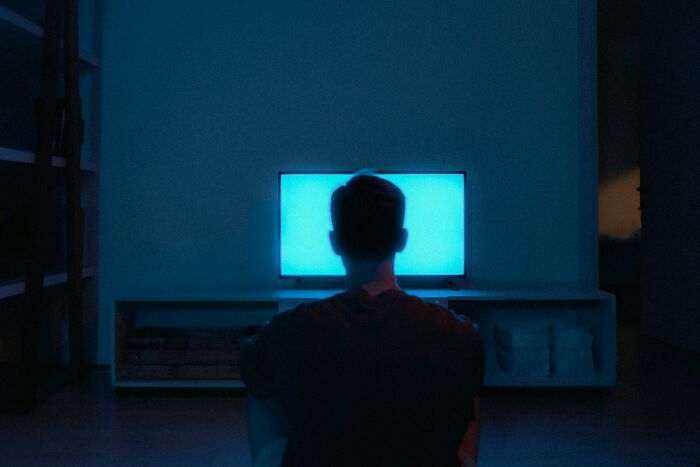 A person watches a bright blue TV screen in a dimly lit room, reflecting on outdated facts and misinformation.