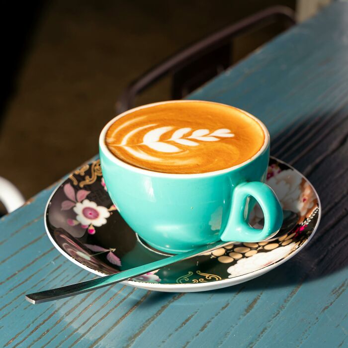 A vibrant turquoise latte cup with beautiful leaf-shaped latte art, on a floral saucer. Dispelling outdated facts.