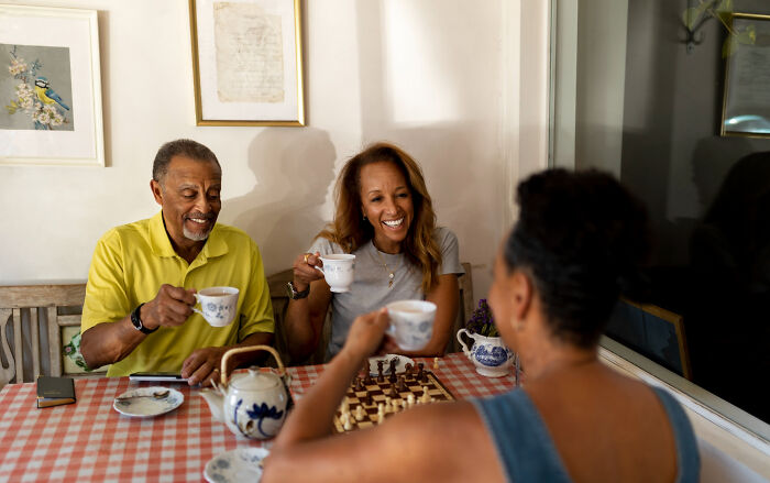 Three people enjoying tea, smiling and playing chess, keeping secrets from their significant others. Brutally honest confessions.