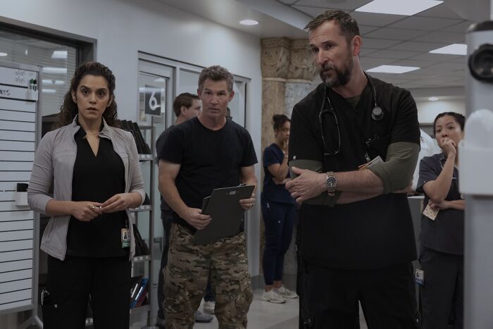 The Pitt star, Noah Wyle, and others stand attentively in hospital hallway The Pitt star, Noah Wyle, and others stand attentively in hospital hallway